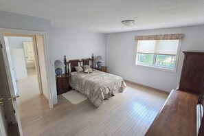 Une chambre à coucher comprenant un lit, des tables de chevet, une fenêtre avec des stores et une porte donnant sur une autre pièce.