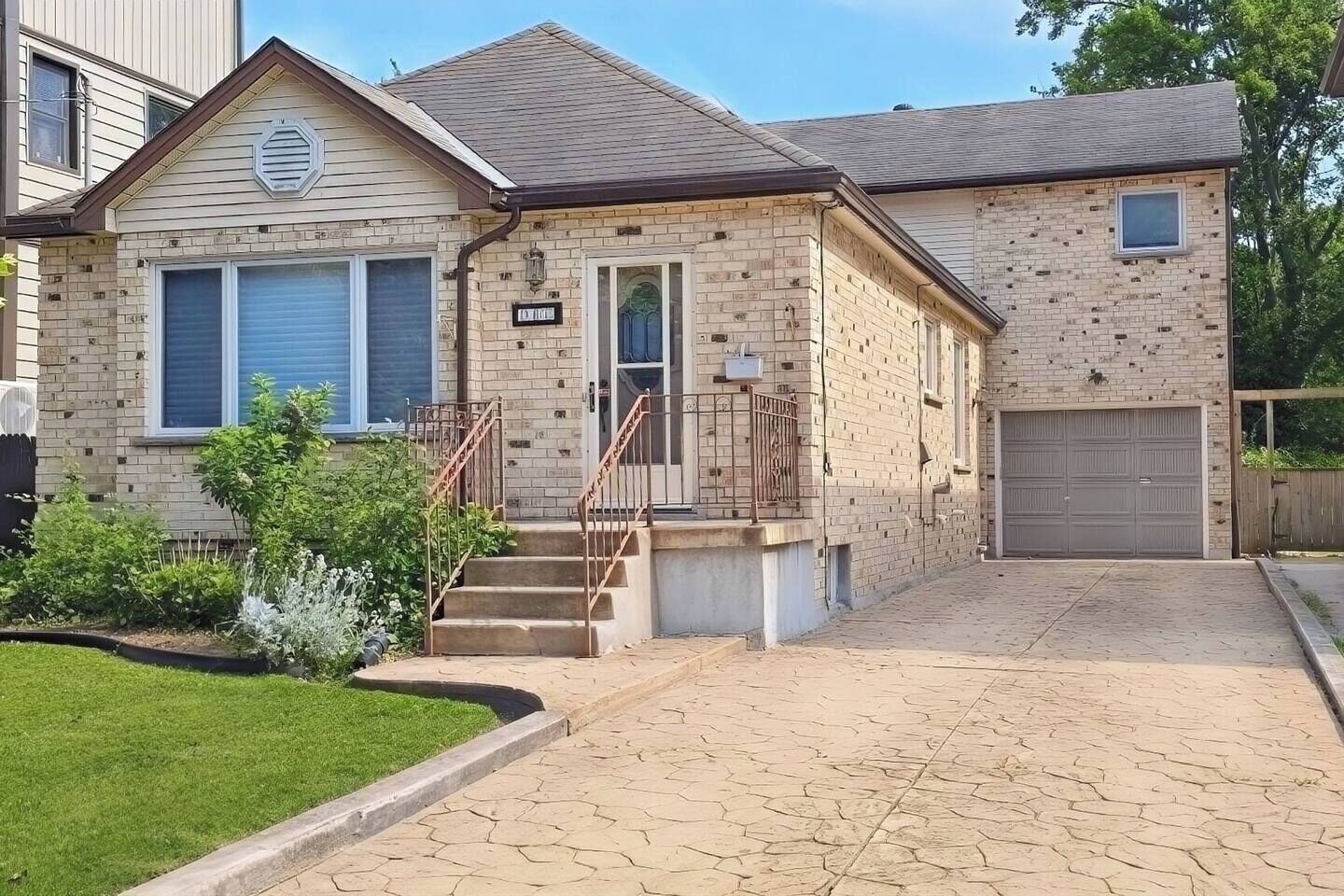 A two-story house with a brick facade, a front garage, and a small front yard with a lawn and shrubs.