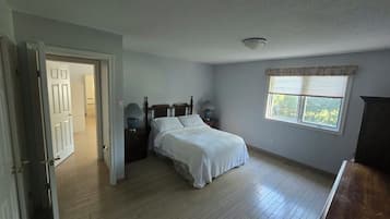 Quarto com cama, mesa de cabeceira, janela com persianas e porta que dá para outro cômodo.