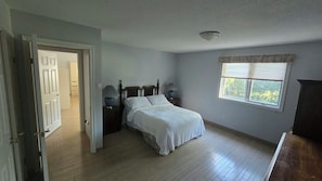 Une chambre à coucher comprenant un lit, une table de chevet, une fenêtre avec des stores et une porte donnant sur une autre pièce.