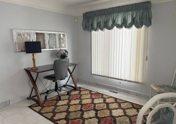 Une pièce comprenant un bureau, une chaise et une fenêtre avec des stores.