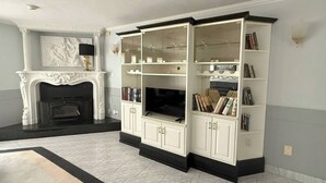 A living room with a fireplace, a large entertainment unit with bookshelves, and a television.