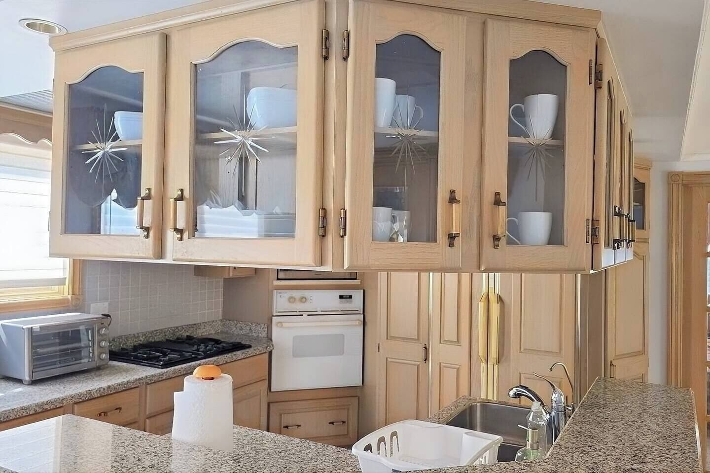 Uma cozinha com armários de madeira, fogão, forno, pia e torradeira.