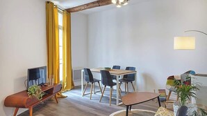 A modern living room with a wooden ceiling, a dining area with a table and chairs, and a television on a wooden stand. - Cozy stay place de la Madeleine (Béziers)