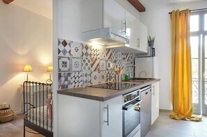 A kitchen with patterned tiles, a stove, oven, and a window with yellow curtains. - Cozy stay place de la Madeleine (Béziers)