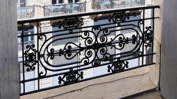 A balcony with ornate black metal railings, a beige building with multiple windows and balconies in the background. - Designer 70sqm flat with les Halles view, A/C (Béziers)