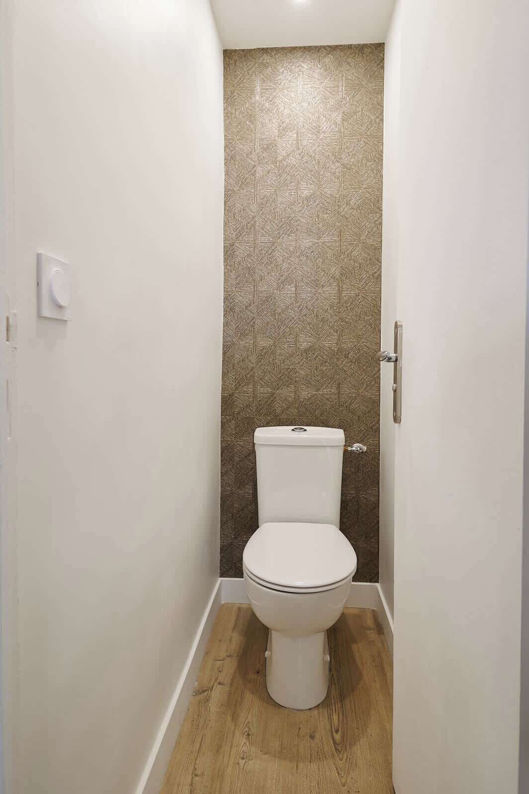 Een kleine, smalle badkamer met een wit toilet, een houten vloer en een structuurwand.