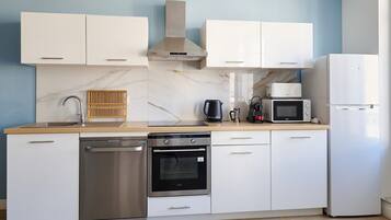 Une cuisine moderne avec des meubles blancs, un lave-vaisselle en acier inoxydable, un four, un four à micro-ondes et un réfrigérateur.