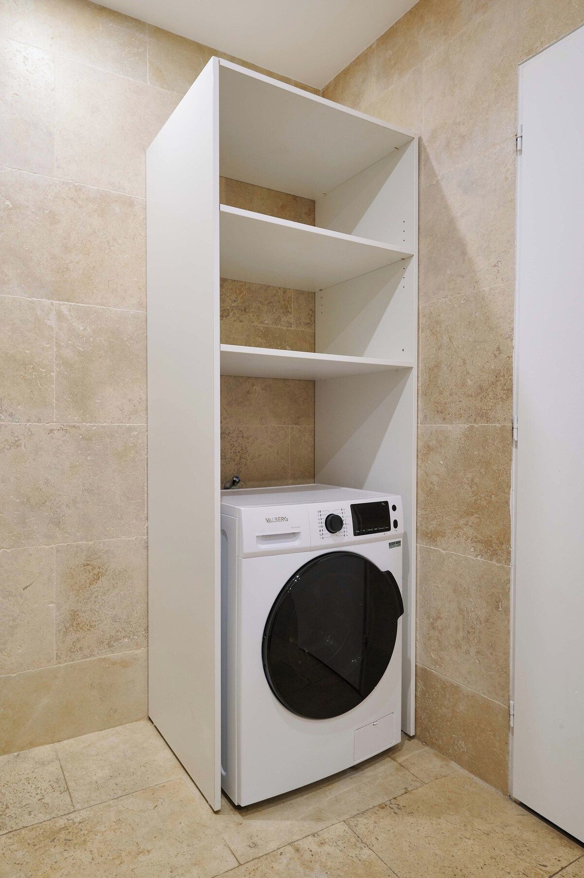 Un cuarto de lavandería con lavadora blanca y estantería empotrada.