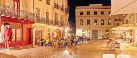 A cobblestone street at night with outdoor seating and buildings on either side.