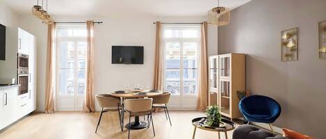 A modern living room with a dining area, a sofa, a TV, and a large window with curtains.