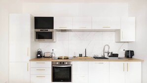 Una cocina moderna con armarios blancos, horno integrado, microondas y cafetera.