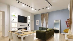 Un espacio de estar moderno con zona de comedor, un sofá verde y un televisor de pantalla plana montado en la pared.