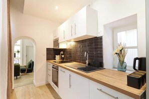 A modern kitchen with white cabinets, a black backsplash, and a wooden countertop. - Appartement de prestige au coeur de Beziers (Béziers)