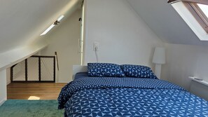 A bedroom with a sloped ceiling, a bed with patterned bedding, a bedside table, a lamp, and a view of the outside.