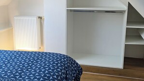Un dormitorio con cama, radiador, suelo de madera y techo inclinado.