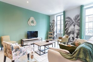 Ein Wohnzimmer mit Fernseher, Sofa, Sessel, Couchtisch und Zimmerpflanzen.