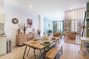 Ein Essbereich mit einem Holztisch, gedeckt für vier Personen, einer Holzbank und Blick auf das Wohnzimmer durch eine Raumtrennung.