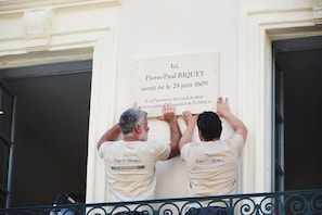 Duas pessoas fixando uma placa comemorativa na fachada de um edifício.