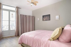 Ein Schlafzimmer mit einem Bett, einem Deckenventilator, einem Fenster mit Vorhängen und zwei gerahmten Bildern an der Wand.