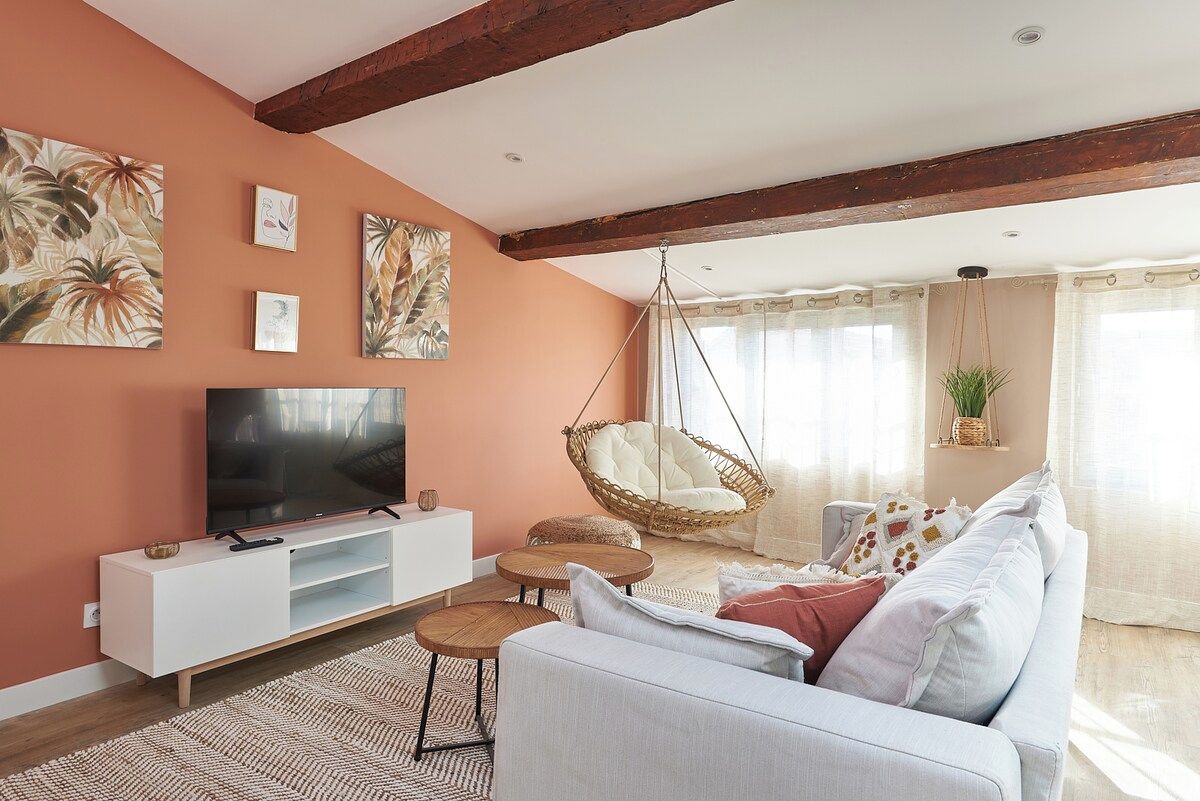 A living room with a white sofa, a hanging chair, a flat-screen TV, and artwork on the wall.