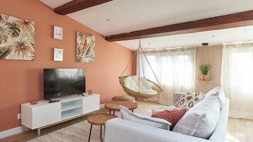 A living room with a white sofa, a hanging chair, a flat-screen TV, and artwork on the wall.