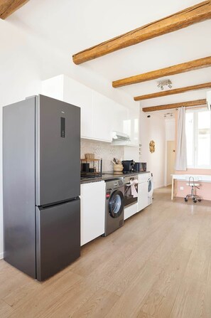 A modern kitchen with a stainless steel refrigerator, a washing machine, and a dining area with a table and chairs. - Le Chic face aux Halles clim  Classe 3 Etoiles (Béziers)