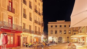 Una strada acciottolata con tavolini all'aperto di un caffè, un edificio con una porta rossa e un cielo notturno sereno.