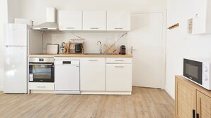 A modern kitchen with white cabinetry, a built-in oven, a dishwasher, and a microwave on a wooden countertop. - Cozy 1BR with A/C across les Halles (Tourcoing)