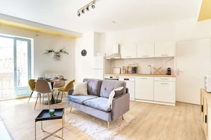 Een modern appartement met een grijze bank, een eettafel en stoelen in de woonkamer, en een keuken met witte kastjes en een koffiezetapparaat.