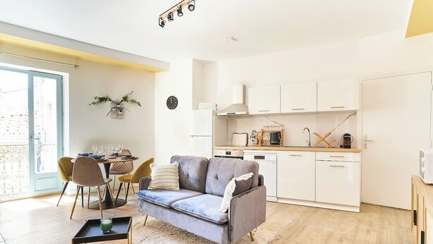 Una cucina moderna con mobili bianchi, un divano grigio e un'area pranzo con sedie gialle.
