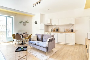 Een moderne keuken met witte kasten, een grijze bank en een eethoek met gele stoelen.