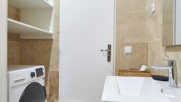 Een badkamer met een wasmachine, een wastafel en een spiegel.