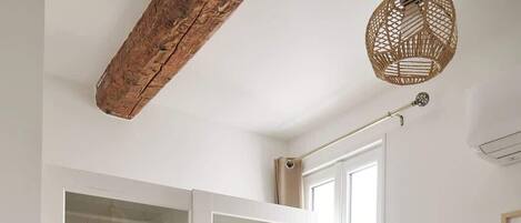 Une pièce avec une armoire blanche, un luminaire suspendu et un lit recouvert d’une couverture marron.