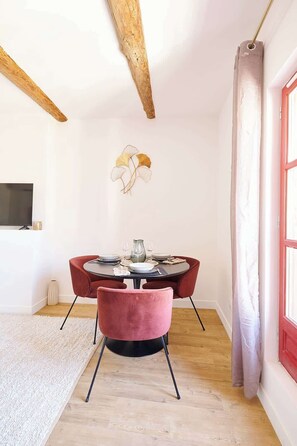 A dining area with a round table, red chairs, a vase, and a wall-mounted artwork. - MyLocTravel ✧ Central, facing Les Halles, AC (Béziers)