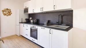 A modern kitchen with white cabinets, a black countertop, a built-in oven, a microwave, and a sink. - MyLocTravel ✧ Central, facing Les Halles, AC (Béziers)