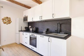 A modern kitchen with white cabinets, a black countertop, a built-in oven, a microwave, and a sink. - MyLocTravel ✧ Central, facing Les Halles, AC (Béziers)
