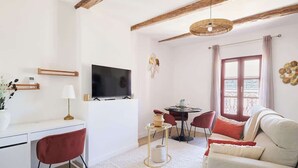 A modern living room with a flat-screen TV, a dining table with chairs, a sofa, and a large window with curtains. - MyLocTravel ✧ Central, facing Les Halles, AC (Béziers)