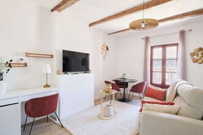 A modern living room with a flat-screen TV, a dining table with chairs, a sofa, and a large window with curtains. - MyLocTravel ✧ Central, facing Les Halles, AC (Béziers)