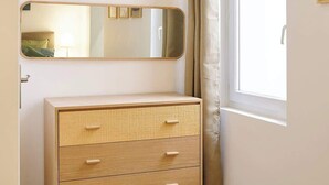 Una habitación con un aparador de madera, un espejo, una ventana con cortinas y un interruptor de luz en la pared.