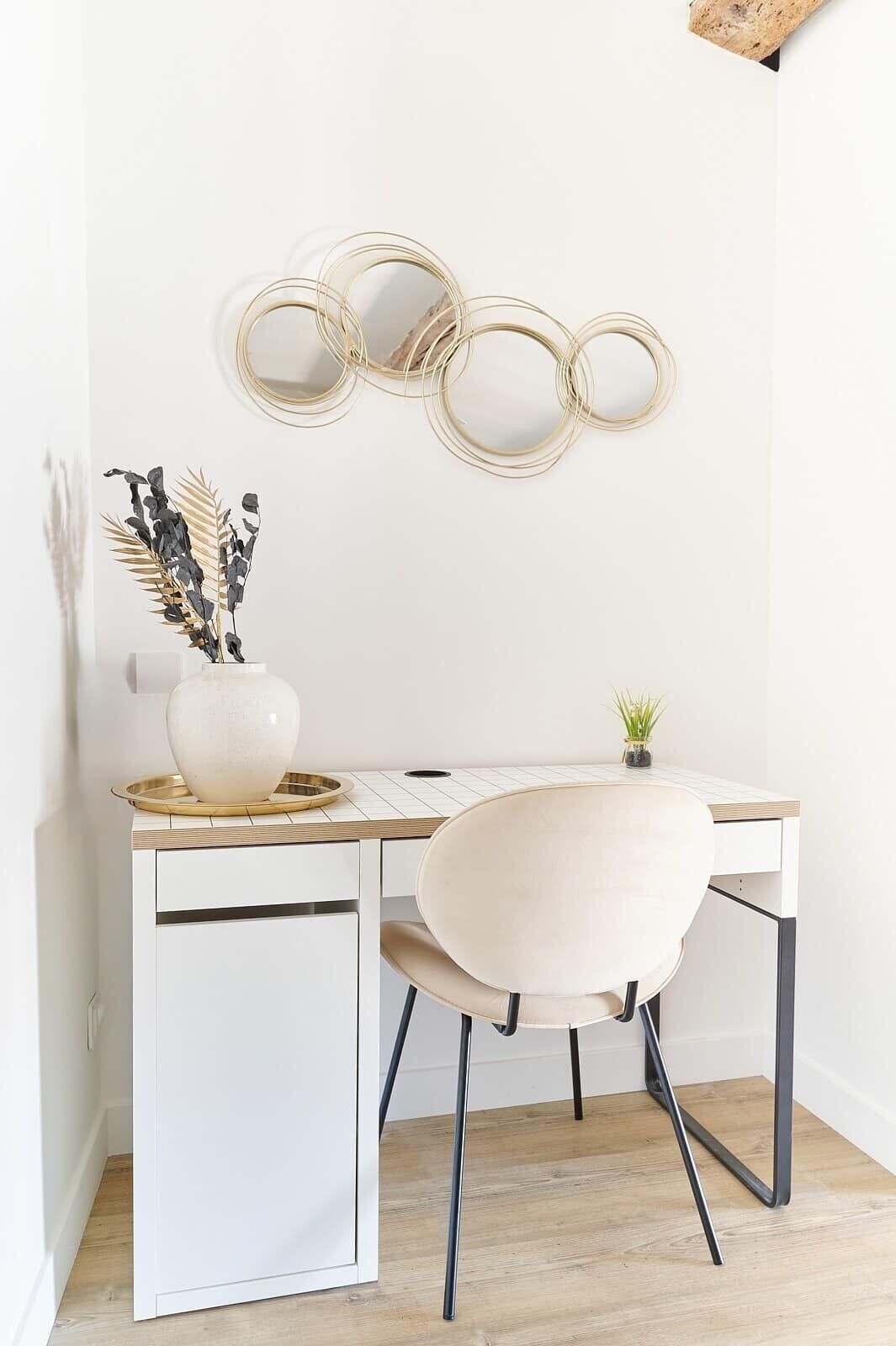 Un bureau blanc orné d’un vase et d’une petite plante, une chaise et un mur décoré de motifs circulaires.