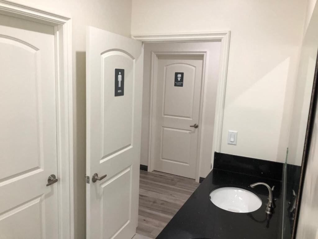 A bathroom with a white sink, a mirror, and a door with a sign.