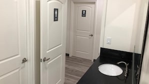 A bathroom with a white sink, a mirror, and a door with a sign. - 8th & Ardmore  (Los Angeles)
