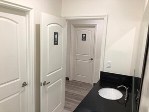 A bathroom with a white sink, a mirror, and a door with a sign. - 8th & Ardmore  (Los Angeles)