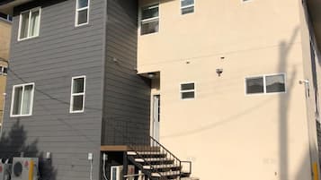 A two-story building with a grey and beige exterior, a visible staircase, and outdoor air conditioning units.