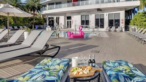 A modern hotel with a pool area, lounge chairs, and a dining setup with food and drinks. - Spacious 1BR - Bay View (Hallandale Beach)