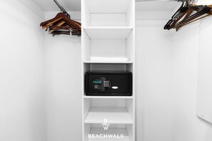Ein weißer Kleiderschrank mit Regalen, einer Kleiderstange und einem schwarzen Tresor.