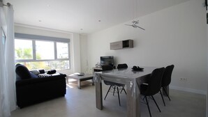 A modern living room with a dining table, black chairs, a sofa, a TV, and a ceiling fan. - Apartment Mirador de Villamartin (Orihuela)