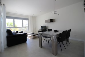 Ein modernes Wohnzimmer mit Esstisch, schwarzen Stühlen, einer Couch, einem Fernseher und einem Deckenventilator.
