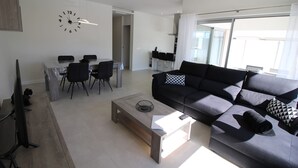 A modern living room with a sofa, coffee table, and dining area. - Apartment Mirador de Villamartin (Orihuela)
